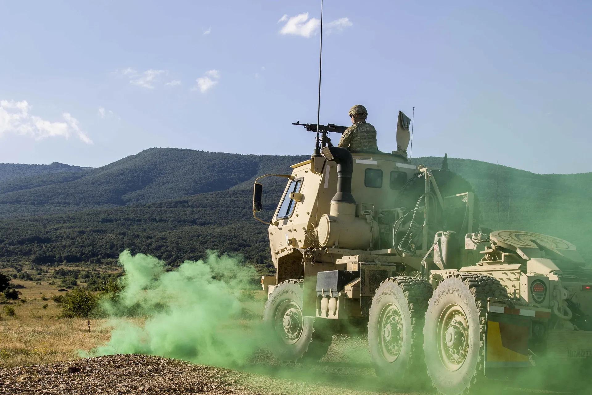 Photo of a military convoy driving over rough terrain, as a green smoke bomb is released under the vehicle - Meeting NATO Standards: How Reusable Boxes Support Defence Compliance